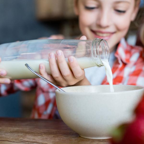 Young child pouring milk into a bowl from a glass bottle