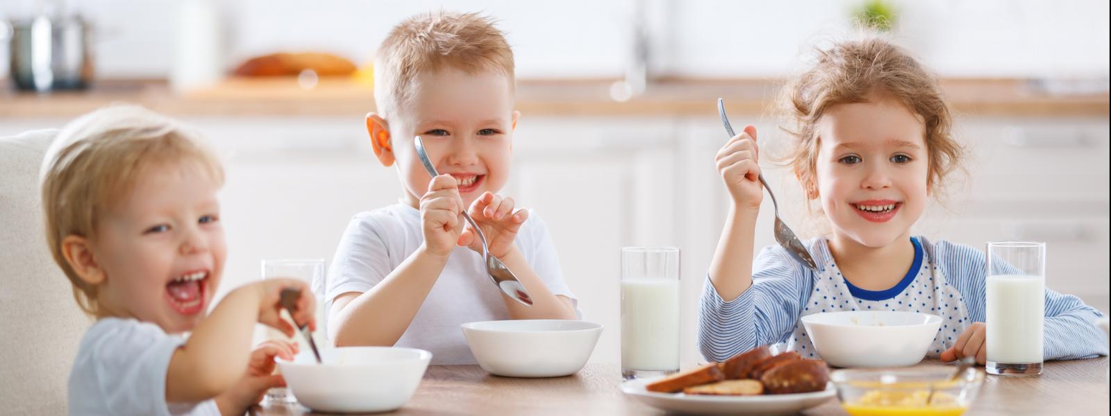 Three children sitting at breakfast table laughing